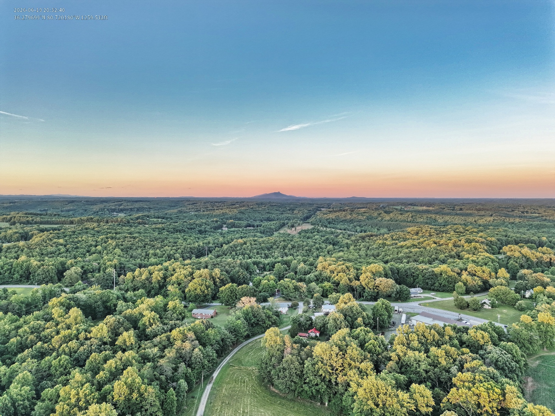 Aerial view over lush green forest with Pilot Mountain at sunset in rural North Carolina